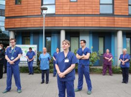 Staff stand outside Salford Royal Hospital in Manchester during a minute's silence to pay tribute to the NHS staff and key workers who have died during the coronavirus outbreak. Image Credits - PA Images/Peter Byrne