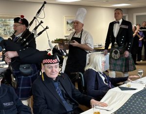 1: Piper Richard France leads chef Gary Alexander and Col (Ret’d) Russ Miller, trustee of Broughton House, into the Burns Supper. Seated, wearing his regimental Glengarry, is Broughton House resident Archie Scott