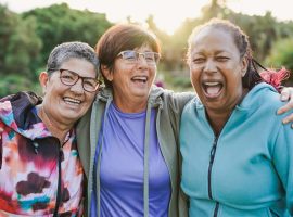 Happy multiracial senior women having fun together outdoor - Elderly generation people hugging each other at city park with sunrise in the background
