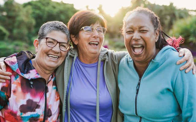Happy multiracial senior women having fun together outdoor - Elderly generation people hugging each other at city park with sunrise in the background
